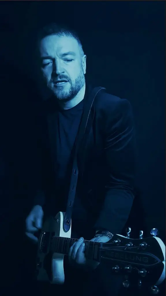 A phopto of the musician Eigenwill in a dark studio setting with a white electric guitar